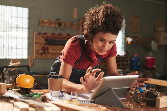 Person beugt sich über einen Tisch in einer Werkstatt und betrachtet ein Tablet.